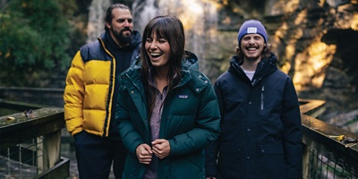 Three smiling hikers wearing cold-weather jackets on a walkway 