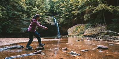 Girl jumping rocks in front of a Waterfall at Hocking Hills