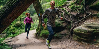 two people running through the woods with trees and rocks behind them