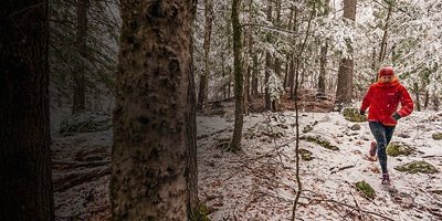Woman in a red jacket trail running in the snow.