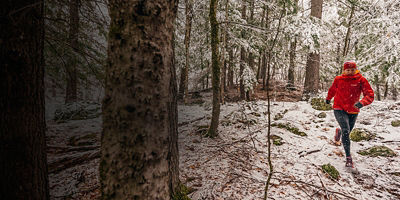 Woman in a red jacket trail running in the snow.