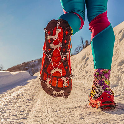 Low angle view of the bottom of trail runner's shoes with microspikes on snow covered trail. Park City, UT