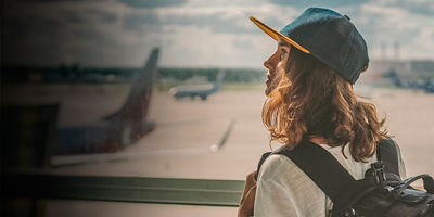 young girl traveler with backpack at the airport on the background of the takeoff field