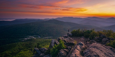 A hiker at the summit of Mary's Rock taking in a gorgeous Summer sunrise in Shenandoah National Park.