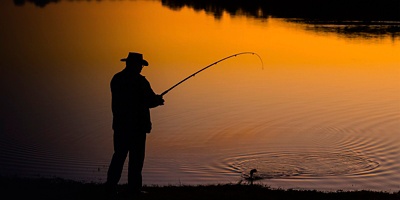 A man fishing from the shore at sunset