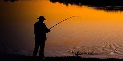 Fishing rod spinning with the line close-up. Fishing rod in rod holder in  fishing boat due the fishery day at the sunset. Fishing rod rings. Fishing  tackle. Fishing spinning reel. Stock Photo