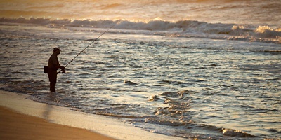 Fisherman at sea fishing during a colorful sunrise at the beach in Robert Moses State Park, Long Island, New York