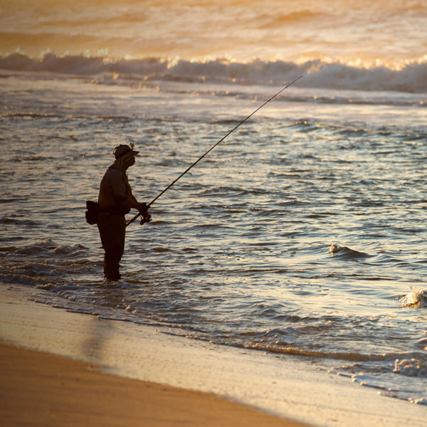 Fisherman at sea fishing during a colorful sunrise at the beach in Robert Moses State Park, Long Island, New York