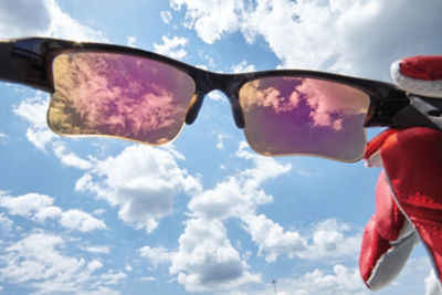 an image of a zoomed in pair of sunglasses held  up against a sunny sky with a few clouds.
