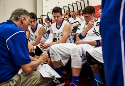 Youth basketball coach discussing game plan with players on the bench.