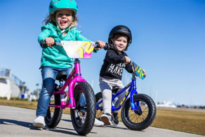 A little girl and boy riding their balance bikes on the sidewalk