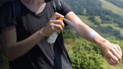 Woman hiker applying Sunscreen spray / sunblock lotion outdoors during summer hike