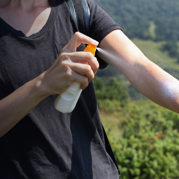 Woman hiker applying Sunscreen spray / sunblock lotion outdoors during summer hike