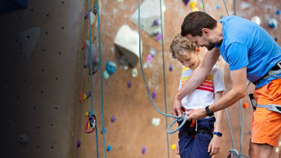 A father and son, preparing for rock climbing together at indoor climbing gym