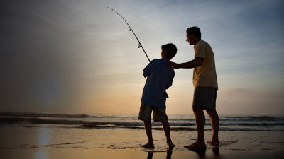 Man and young boy fishing in surf