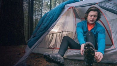 A mountain biker puts biking shoes on outside his tent