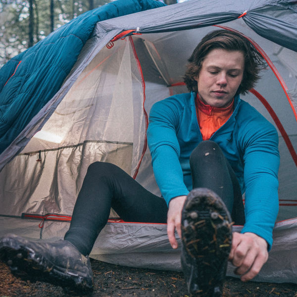 A mountain biker puts biking shoes on outside his tent