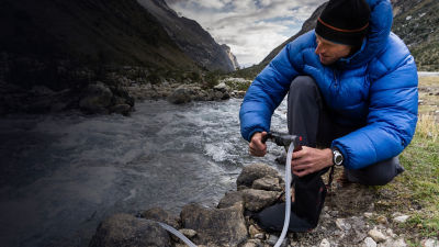 man in blue down jacket filtering water from a river for drinking and cooking 