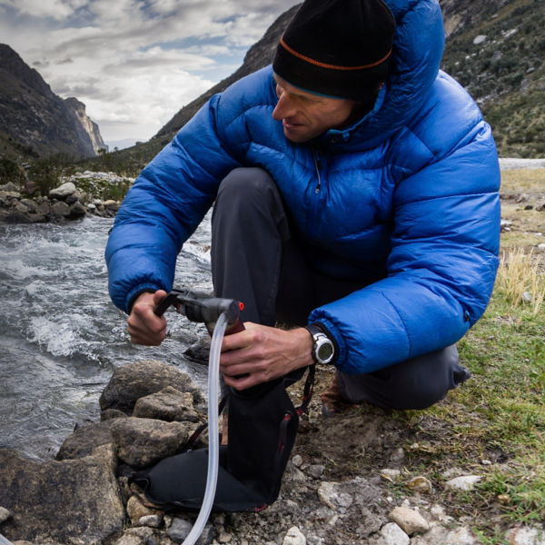 man in blue down jacket filtering water from a river for drinking and cooking 