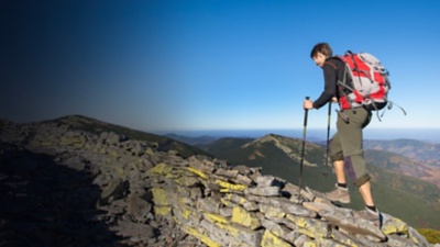 A woman walking on the rocky ridge of the mountain with beautiful high altitude landscape view on the background