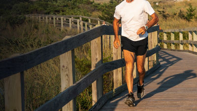 A man is running at the beach on a boardwalk with beach gras and dunes in the background.