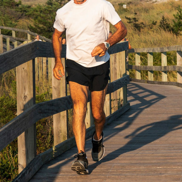 A man is running at the beach on a boardwalk with beach gras and dunes in the background.