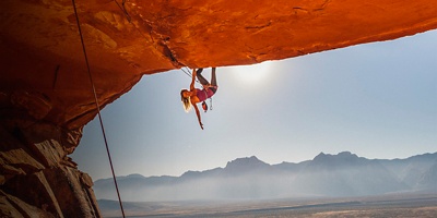 A photo of Heather Weidner hanging from a climb being belayed by Chris Weidner