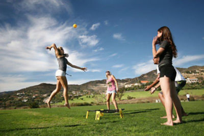 Four people playing spikeball in a field on a sunny day