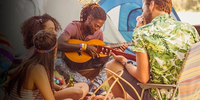 A group of friends sit around their tents while camping playing music
