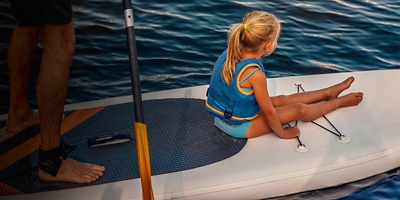 A father paddles on a SUP while a little girl rides on the front