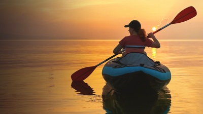 Red-haired young woman is rowing on an inflatable kayak by the sea with a dog Jack Russell Terrier on a background of pink sunrise in beautiful nature. Great disk of the rising sun. Sun rays. Sport, Red-haired young woman is rowing on an inflatable kayak by the s