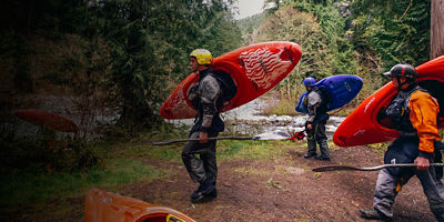 Kayakers approach a river with their dry suits
