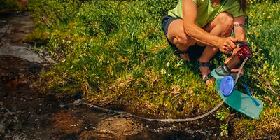 Woman filtering drinking water from an alpine stream in the Cirque of the Towers, Wind River Range, Popo Agie Wilderness area, Wyoming