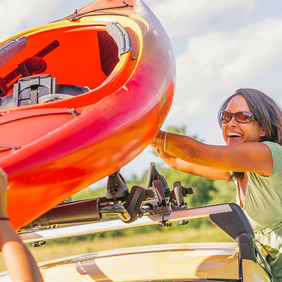 A woman puts a kayak on top of her car on a roof rack