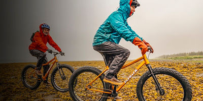 Two men bike in the rain through a kelp covered section of beach in the Kenai Fjords National Park.