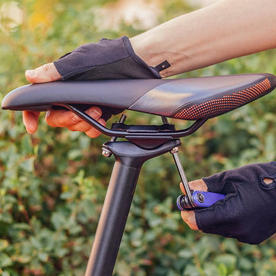A hand with a multitool twists the mount on a bike saddle 