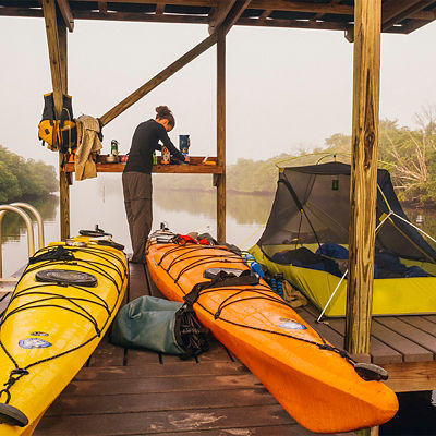A woman makes coffee while camped on a chickee in Everglades National Park during a backcountry kayak trip.