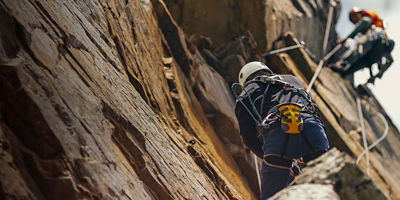 A lead climber belays a lower climber on a rockface