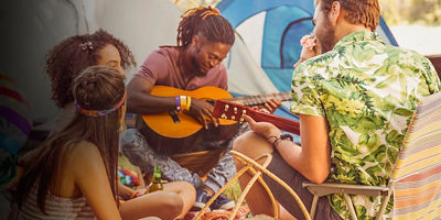 A group of friends sit around their tents while camping playing music