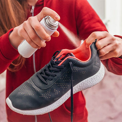 A young woman spraying deodorant on sweaty running shoes for eliminate unpleasant, bad smell. Shoe shine and care. Sport footwear needs in cleaning and odor removal.