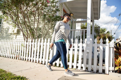 woman walking down the sidewalk listening to music with a white fence in the background