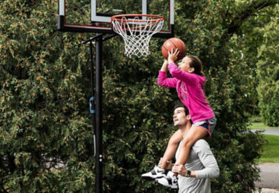 Daughter shooting a basketball while being held on her dad's shoulders