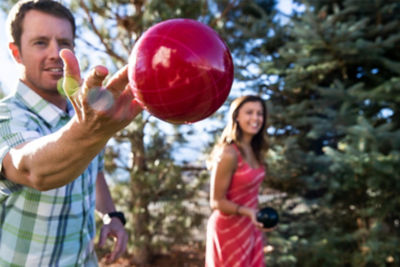 Man throwing red bocce ball with woman watching in the background