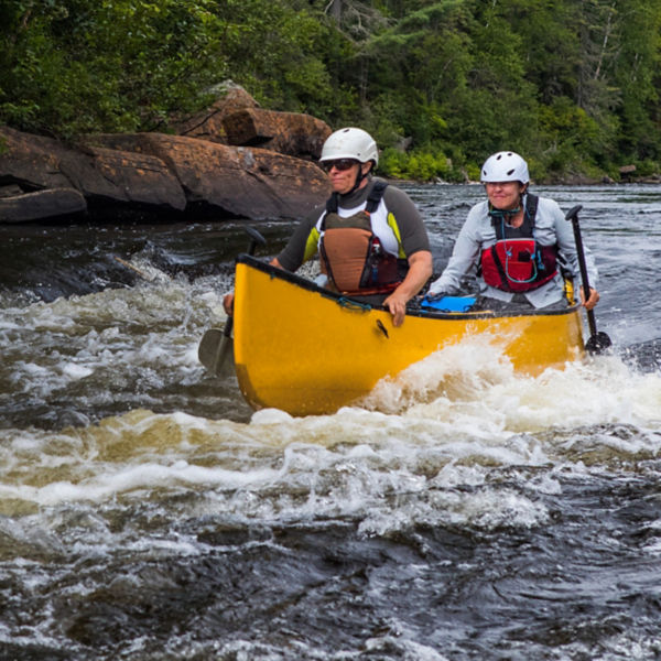A group of people paddling in whitewater with a canoe