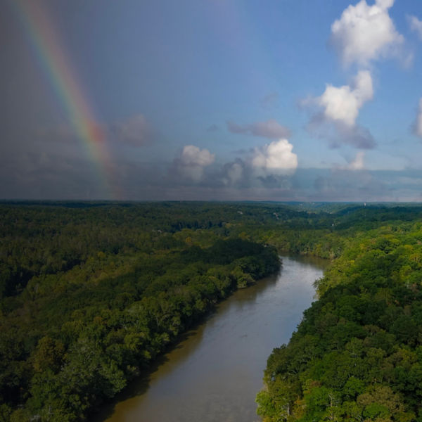 The Chattahoochee river surrounded by lush green and autumn colored trees with blue sky, a rainbow and clouds at Cochran Shoals Trail in Marietta 