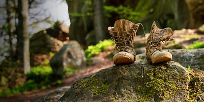 Well-worn hiking boots, unlaced and muddy on the forest floor.