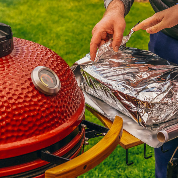 A Man and woman making food together on a red Kamado Barbecue Grill.  