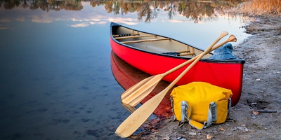 red tandem canoe with a wooden paddles and a dry bag on a lake shore