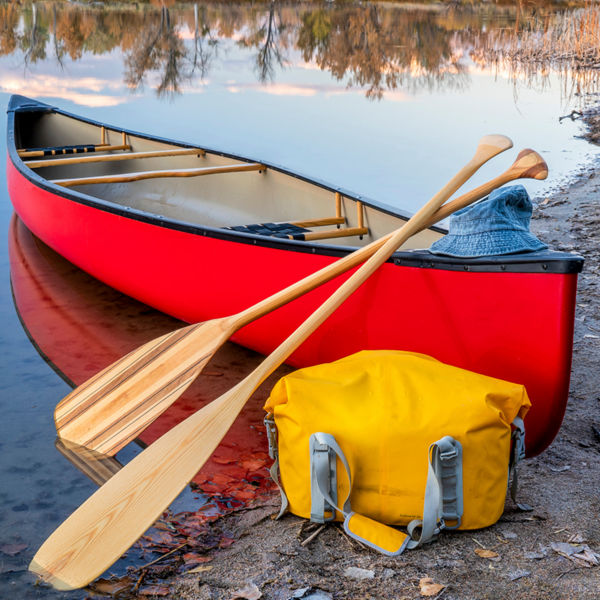 red tandem canoe with a wooden paddles and a dry bag on a lake shore