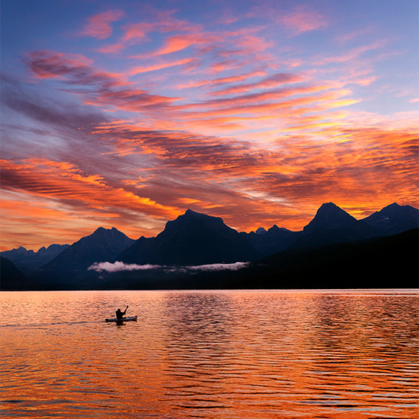 A kayaker paddles across Lake MacDonald at sunrise in Glacier National Park, Montana, USA.